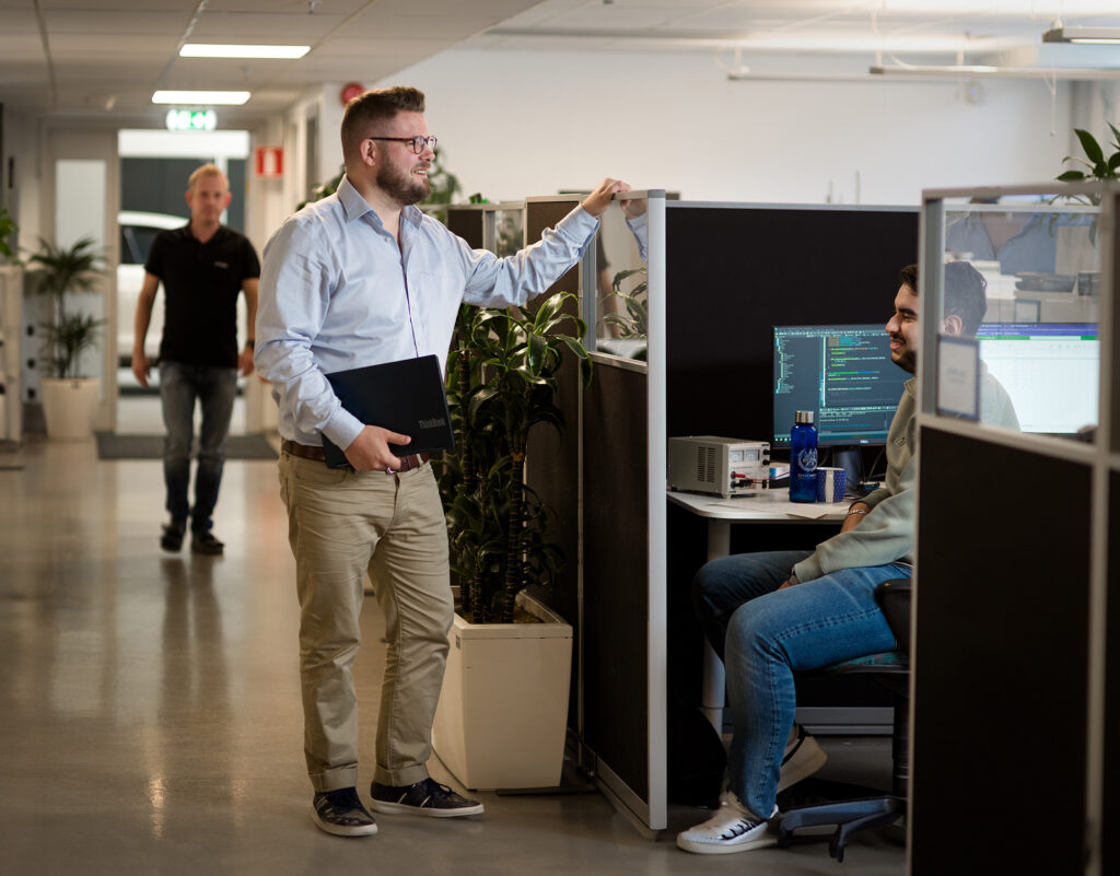 En säljare står och pratar med en medarbetare som sitter vid en dator.